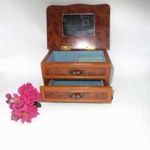 Peut inclure: Une bo&icirc;te &agrave; bijoux en bois avec un couvercle &agrave; charni&egrave;res et un miroir &agrave; l'int&eacute;rieur. La bo&icirc;te a deux tiroirs avec des poign&eacute;es en laiton. La bo&icirc;te est brune avec un motif de grain de bois.