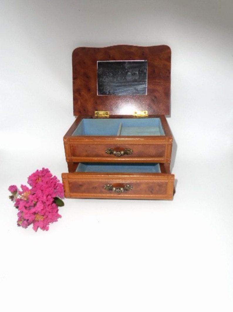 Peut inclure: Une bo&icirc;te &agrave; bijoux en bois avec un couvercle &agrave; charni&egrave;res et un miroir &agrave; l'int&eacute;rieur. La bo&icirc;te a deux tiroirs avec des poign&eacute;es en laiton. La bo&icirc;te est brune avec un motif de grain de bois.