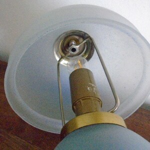 May include: A blue glass lampshade with a frosted glass top and a gold metal base. The lampshade is attached to a metal frame with a light bulb inside.