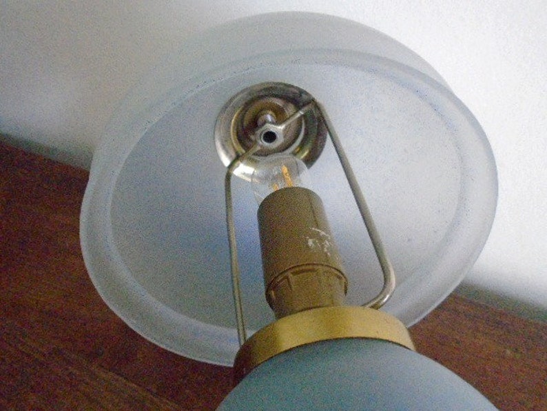 May include: A blue glass lampshade with a frosted glass top and a gold metal base. The lampshade is attached to a metal frame with a light bulb inside.