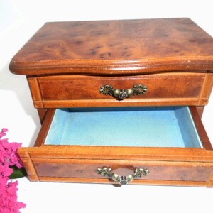 Peut inclure: Une bo&icirc;te &agrave; bijoux en bois avec deux tiroirs. Le tiroir sup&eacute;rieur est ferm&eacute; et le tiroir inf&eacute;rieur est ouvert, r&eacute;v&eacute;lant une doublure en velours bleu. La bo&icirc;te a un motif de grain de bois et des poign&eacute;es en m&eacute;tal orn&eacute;es.