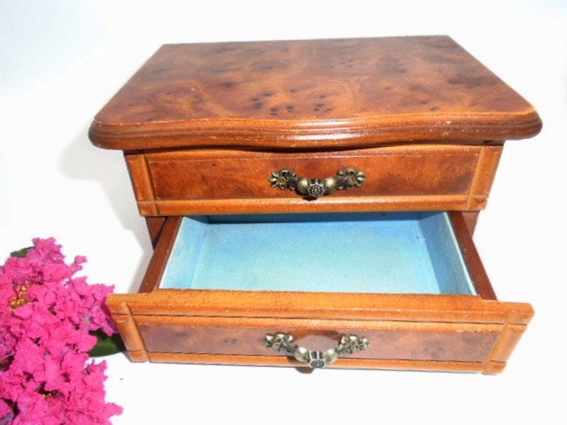 Peut inclure: Une bo&icirc;te &agrave; bijoux en bois avec deux tiroirs. Le tiroir sup&eacute;rieur est ferm&eacute; et le tiroir inf&eacute;rieur est ouvert, r&eacute;v&eacute;lant une doublure en velours bleu. La bo&icirc;te a un motif de grain de bois et des poign&eacute;es en m&eacute;tal orn&eacute;es.