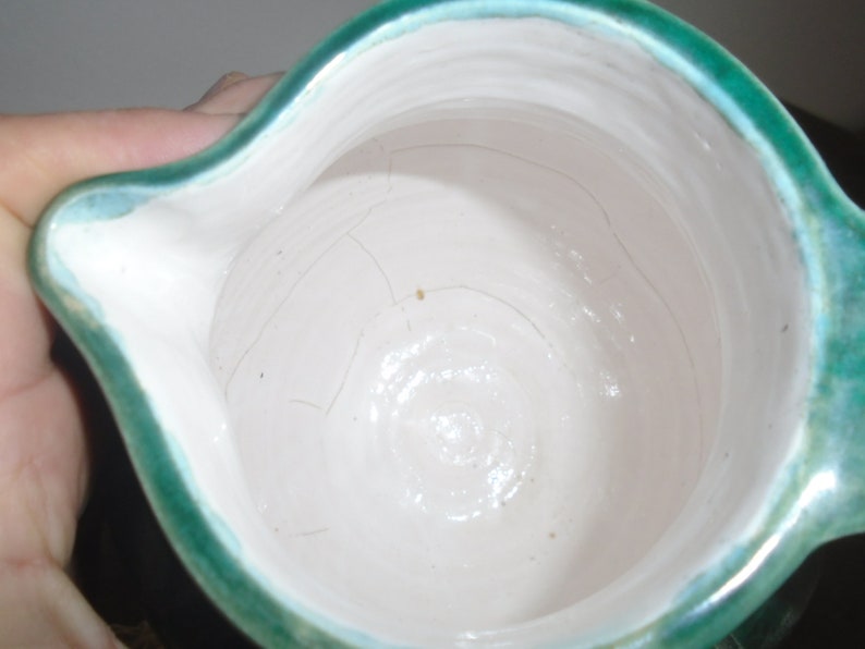 Peut inclure: Un pichet en c&eacute;ramique blanche avec un bord et un gla&ccedil;age verts. Le pichet a une large ouverture et une anse.