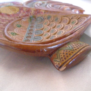 May include: A brown ceramic dish with a decorative design of colorful flowers and leaves. The dish is shaped like a bird with a long tail.
