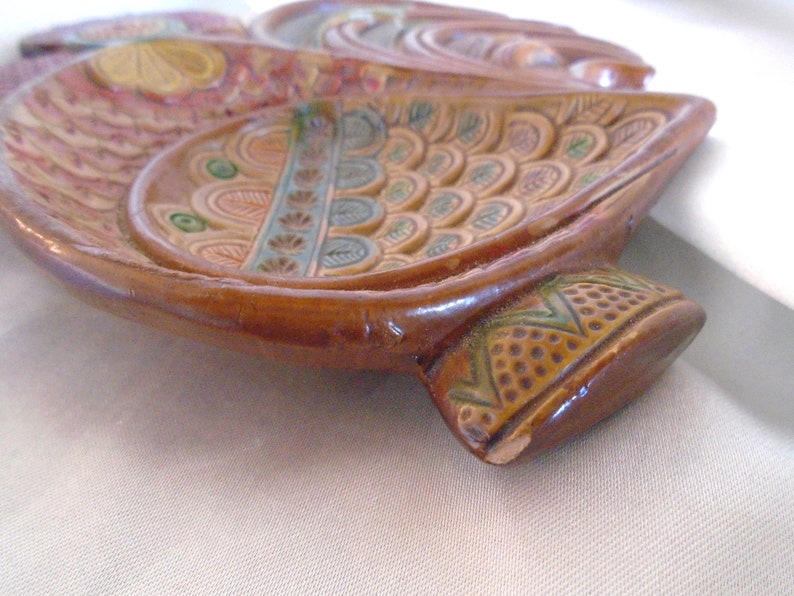 May include: A brown ceramic dish with a decorative design of colorful flowers and leaves. The dish is shaped like a bird with a long tail.