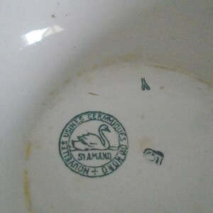 May include: Close-up of a green and white ceramic mark with a swan and the text "Usines Ceramiques De St Amand + Quievrain".