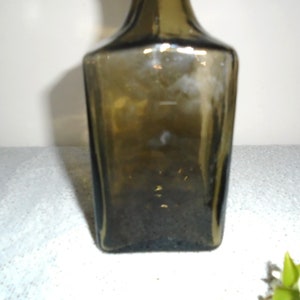 May include: A dark green glass bottle with a square shape.