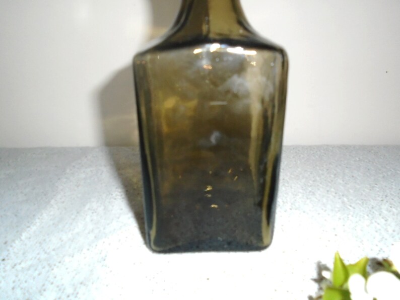 May include: A dark green glass bottle with a square shape.