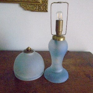 May include: Two frosted glass lamps with brass accents. The lamp on the left is a dome-shaped lamp with a brass finial. The lamp on the right is a tall, slender lamp with a brass cage around the bulb.