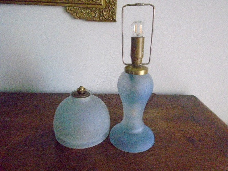 May include: Two frosted glass lamps with brass accents. The lamp on the left is a dome-shaped lamp with a brass finial. The lamp on the right is a tall, slender lamp with a brass cage around the bulb.