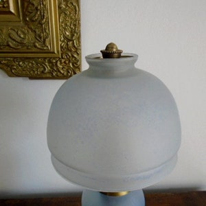 May include: A frosted glass lampshade with a brass finial. The lampshade is a light blue color and has a slightly textured surface.