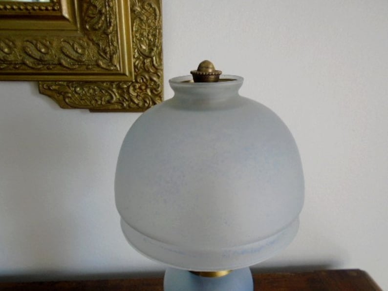 May include: A frosted glass lampshade with a brass finial. The lampshade is a light blue color and has a slightly textured surface.