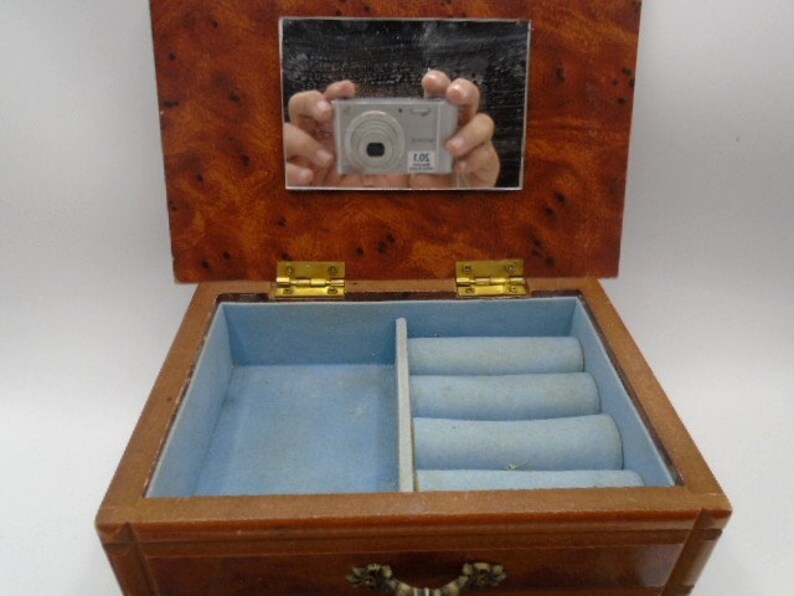 Peut inclure: Une bo&icirc;te &agrave; bijoux en bois avec un couvercle &agrave; charni&egrave;res et un miroir &agrave; l'int&eacute;rieur. La bo&icirc;te est en bois brun clair et a une doublure en velours bleu. La bo&icirc;te a un petit tiroir en bas.