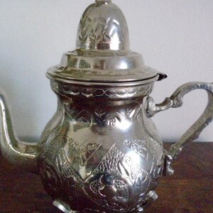 Puede incluir: Una tetera de plata con un dise&ntilde;o ornamentado y una tapa. La tetera tiene un pico y una manija.