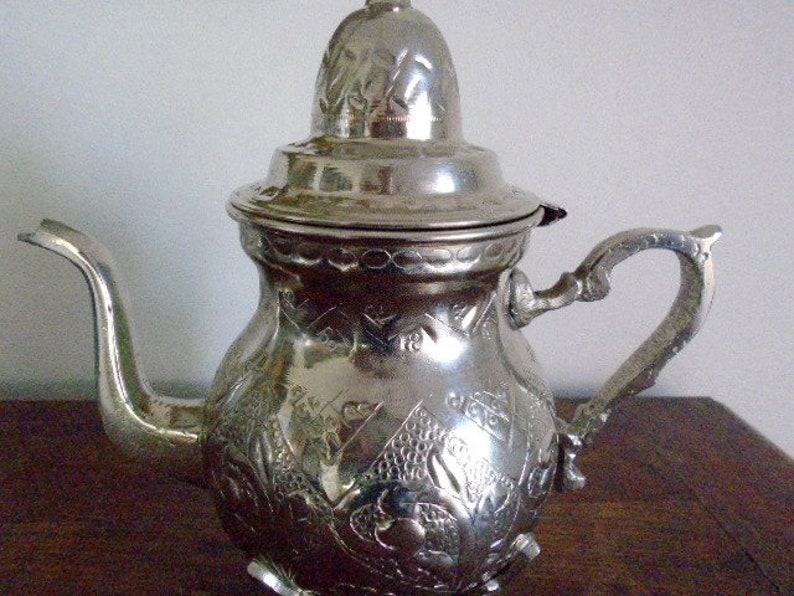 Puede incluir: Una tetera de plata con un dise&ntilde;o ornamentado y una tapa. La tetera tiene un pico y una manija.