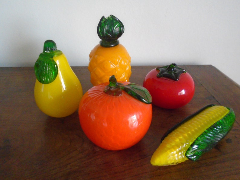 May include: A set of five glass fruit sculptures, including a pineapple, pear, orange, tomato, and corn. The sculptures are all brightly colored and have realistic details.
