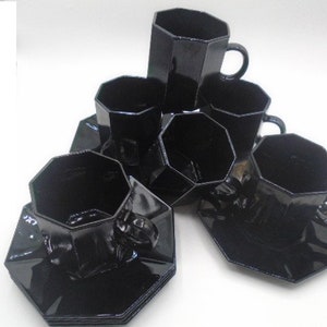 May include: Set of six black octagonal glass teacups and saucers. The cups and saucers are all the same shape and size, and they are all made of a dark, opaque glass.