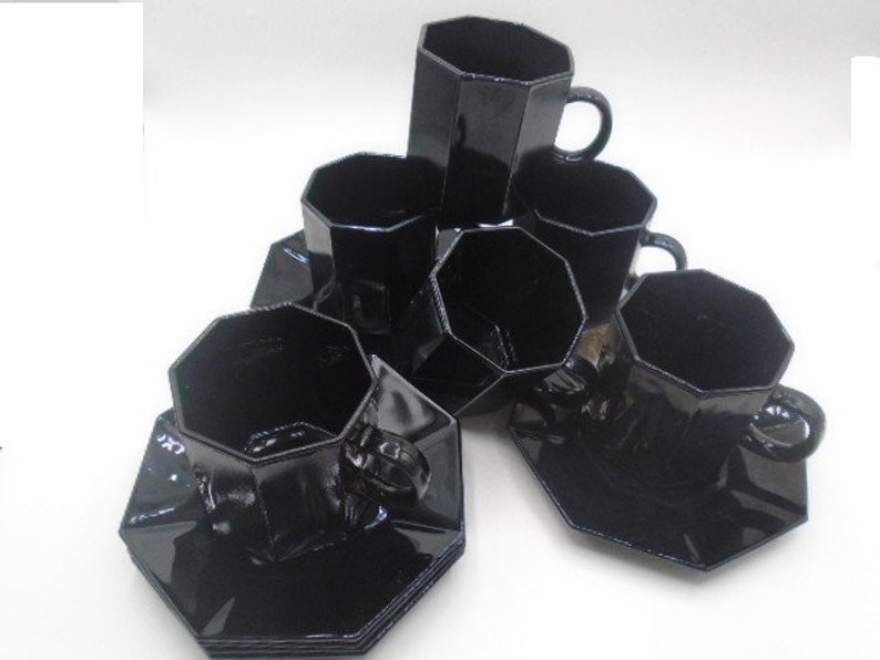 May include: Set of six black octagonal glass teacups and saucers. The cups and saucers are all the same shape and size, and they are all made of a dark, opaque glass.