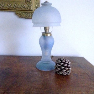 May include: A frosted glass table lamp with a blue base and a white frosted glass shade. The lamp is sitting on a wooden surface.