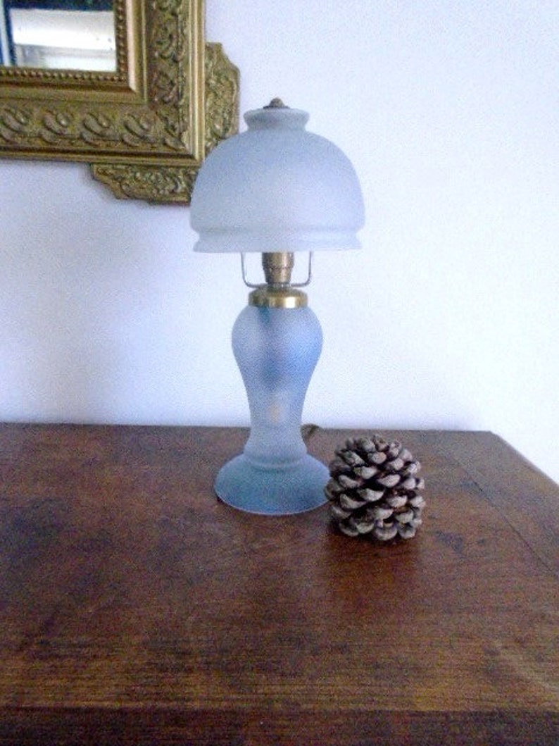 May include: A frosted glass table lamp with a blue base and a white frosted glass shade. The lamp is sitting on a wooden surface.