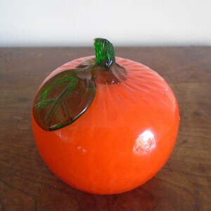 May include: A glass orange with a green leaf, a decorative piece for a home or office.