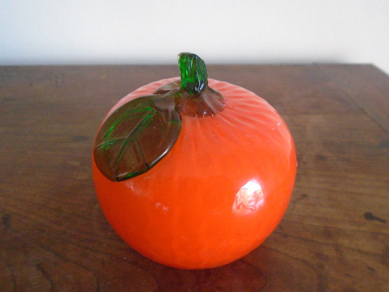 May include: A glass orange with a green leaf, a decorative piece for a home or office.