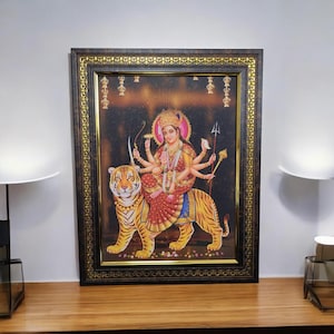 May include: A framed print of a Hindu goddess, Durga, riding a tiger. She has eight arms and is holding various weapons and symbols. The print is set against a dark background with gold accents.