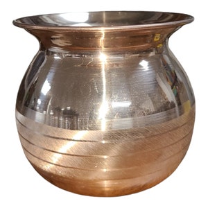May include: A shiny, copper-colored, round, metal pot with a wide, flat rim and horizontal lines around the body.