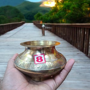 May include: A gold-colored brass pot with intricate floral designs. The pot has a sticker with the number "8" on it.