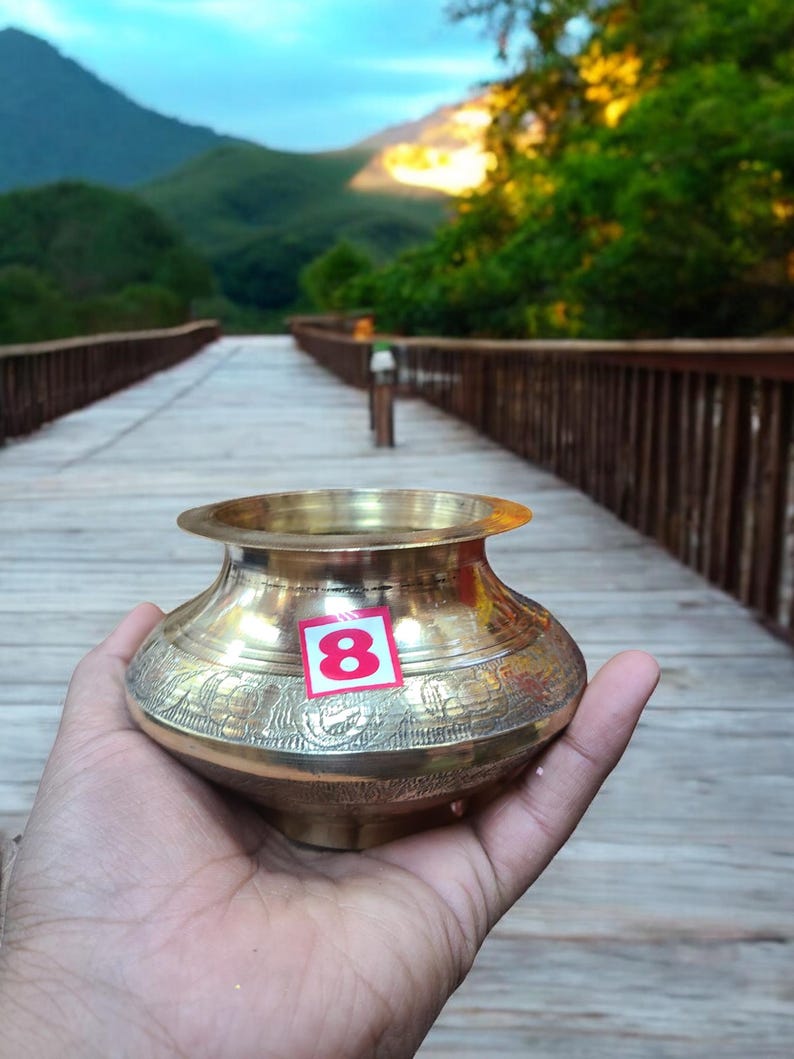 May include: A gold-colored brass pot with intricate floral designs. The pot has a sticker with the number "8" on it.