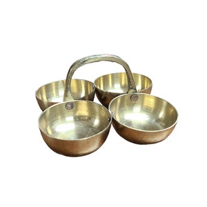 May include: A brass serving dish with four round bowls and a curved handle. The bowls are arranged in a cloverleaf pattern, and the handle is attached to the top of the bowls. The brass has a polished finish.