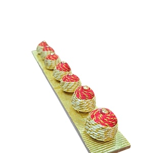 May include: A row of eight small, round, decorative ornaments with a red and gold striped pattern. The ornaments are arranged on a gold, textured surface.