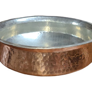 May include: A hammered copper bowl with a silver interior. The bowl has a rounded shape and a wide rim.