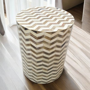 Op de afbeelding: Een ronde bijzettafel met een chevron-patroon gemaakt van botinleg. De tafel is wit en bruin en heeft een cilindrische vorm.