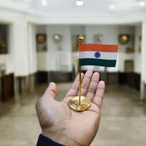 May include: A small golden flag stand with the Indian flag on it. The flag is orange, white, and green with a blue wheel in the center.