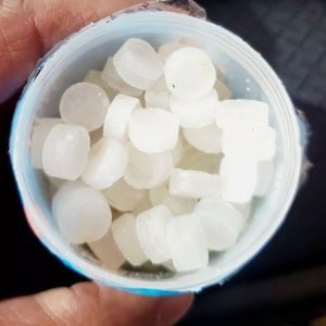 May include: A close-up of a white plastic container filled with small, round, white tablets.