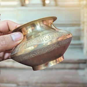 May include: A small, ornate brass bowl with intricate designs. The bowl is held in a hand, and the background is blurred.