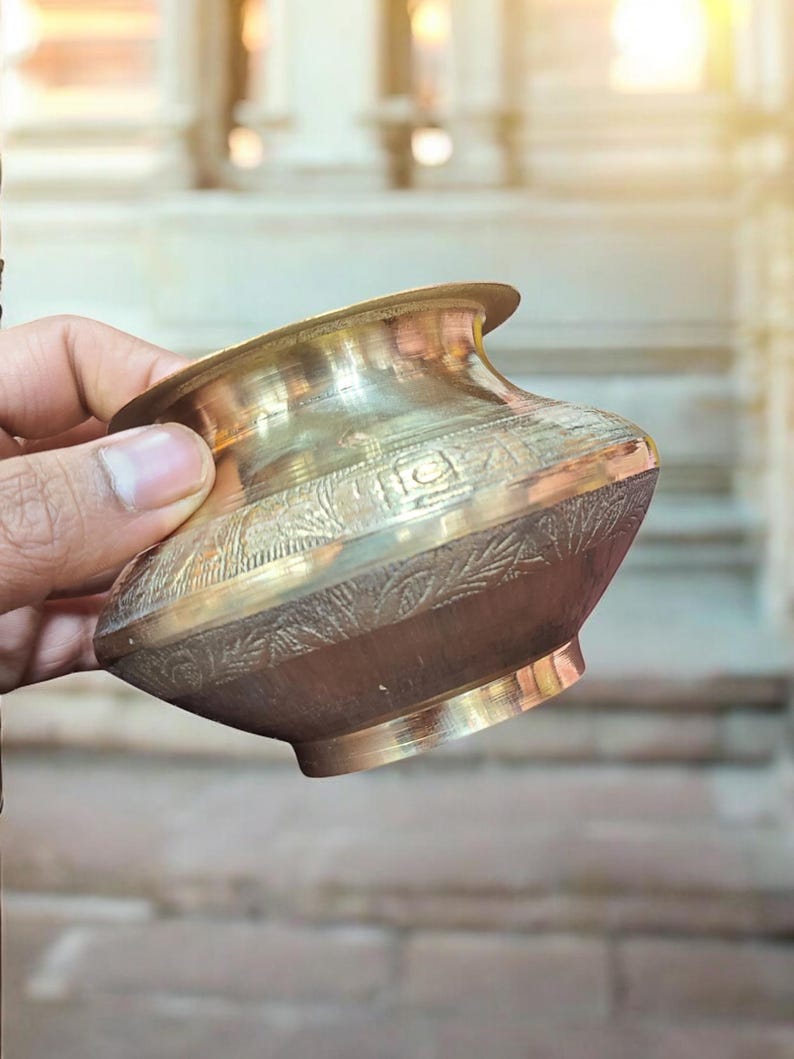 May include: A small, ornate brass bowl with intricate designs. The bowl is held in a hand, and the background is blurred.