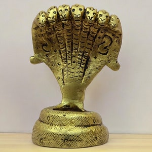 May include: A gold-colored metal statue of a seven-headed cobra, also known as a naga, with a coiled base. The statue is a traditional Hindu symbol of protection and prosperity.