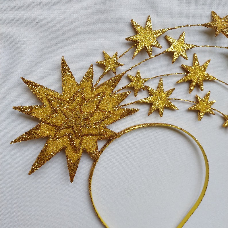 May include: A gold headband with a large glitter star and smaller glitter stars attached to it. The headband is made of a thin, flexible material.