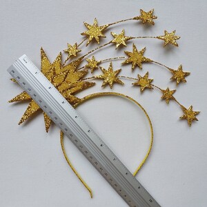 May include: Gold glitter star headband with a large star in the center and smaller stars trailing behind it. The headband is yellow and measures approximately 7 inches in diameter.