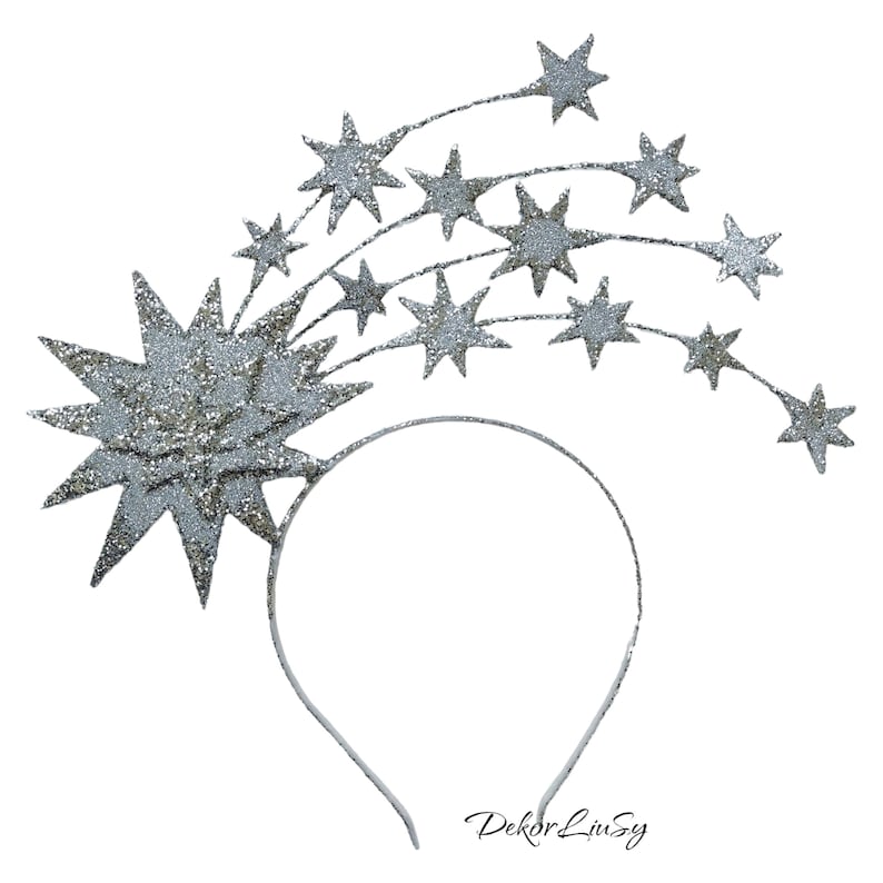 May include: Silver glitter star headband with a large star in the center and smaller stars trailing behind it. The headband is white and has the text "Dekor Livsy" printed on it.