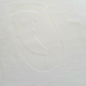 May include: A white textured surface with a raised, oval-shaped impression. The impression is slightly off-center and appears to be a handprint.