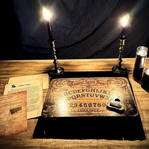 May include: A wooden Ouija board with the words "Haunted Spirit Board" and the alphabet. Two lit candles in ornate holders flank the board. Beside the board are aged papers and a planchette.
