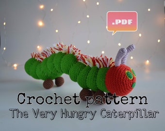 May include: Crochet pattern for The Very Hungry Caterpillar. The pattern is available as a PDF download. The image shows a green crocheted caterpillar with a red head and white and yellow accents.