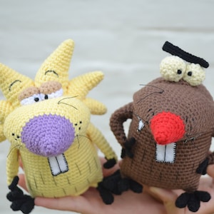 May include: Two crocheted stuffed animals, one yellow with a purple nose and the other brown with a red nose. Both have white teeth and black eyes.