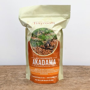 May include: A bag of brown Akadama soil aggregate for plants. The bag is beige with the text "Tinyrools" and "SOIL AGGREGATE AKADAMA - AIDS AND PROMOTES HEALTHY ROOT GROWTH" printed on it. The bag contains 2.25 quarts (2.48L) of soil.