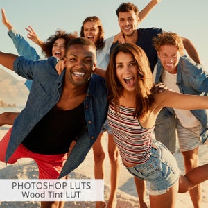 May include: A group of friends laughing and smiling on a beach. They are all wearing casual clothing and have their arms around each other. The image is bright and sunny, and the friends look happy and carefree.