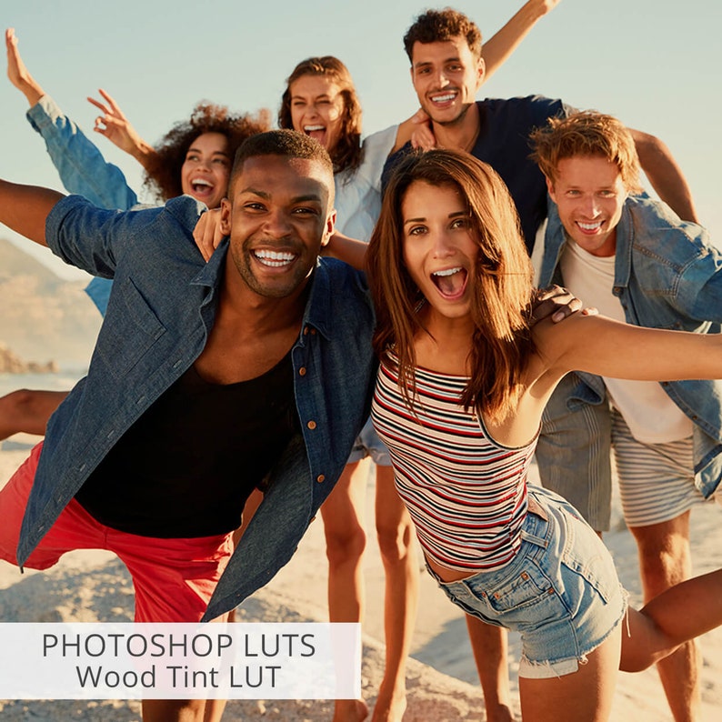May include: A group of friends laughing and smiling on a beach. They are all wearing casual clothing and have their arms around each other. The image is bright and sunny, and the friends look happy and carefree.
