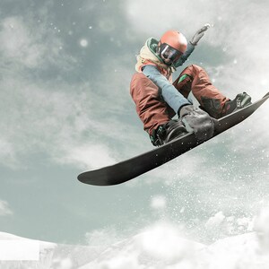May include: A person wearing a helmet and winter clothing is snowboarding in the air. The snowboarder is performing a trick with their body in a crouched position. The background is a cloudy sky with snow falling.